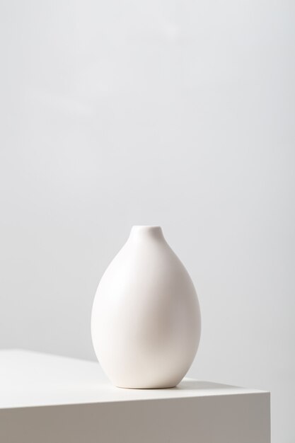 vertical closeup of a white clay vase on the table under the lights against a white