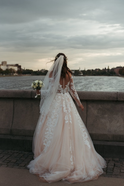 橋の上に立っている白いガウンとウェディングドレスを着ている花嫁の垂直方向の全身ショット