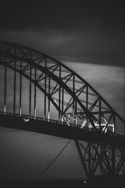 Vertical grayscale shot of a modern iron  arch-shaped bridge