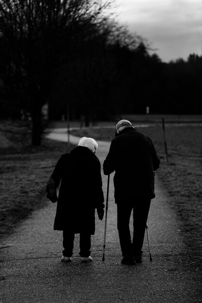 Vertical grayscale shot of old spouses walking in the park  - aging concept