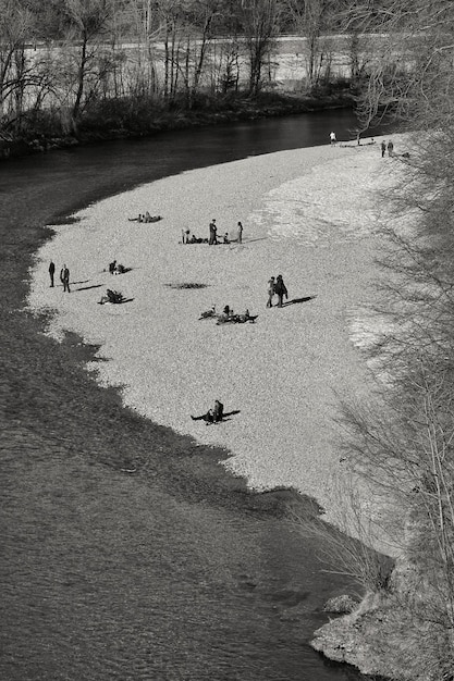 Free photo vertical grayscale shot of people relaxing in a park by the river in winter