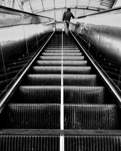 Vertical grayscale shot of a person standing on an escalator