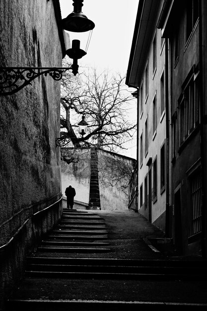 Vertical grayscale shot of a staircase between two buildings leading to upwards