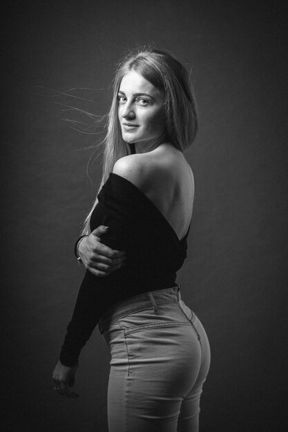 Vertical greyscale shot of an attractive blonde female posing while sitting on a barstool