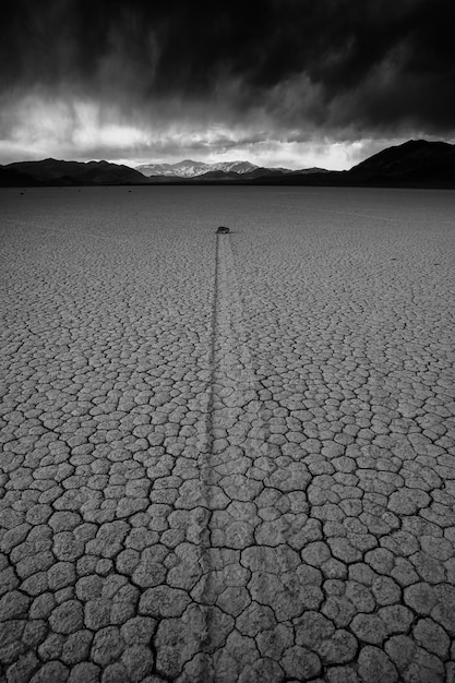Vertical greyscale shot of a deserted ground of sand surrounded by a mountainous scenery