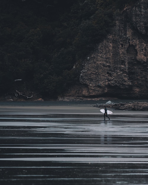 Vertical greyscale shot o a person getting into the water with a surfing desk