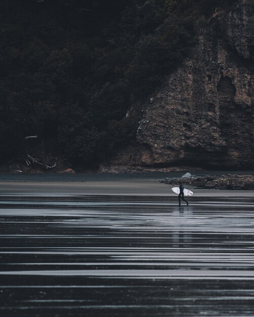 Вертикальный полутоновый снимок человека, садящегося в воду со стола для серфинга