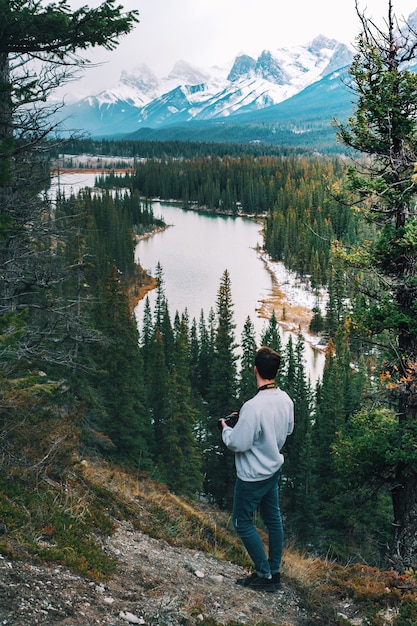 Vertical high angle of a male photographer standing on the cliff and watching the river