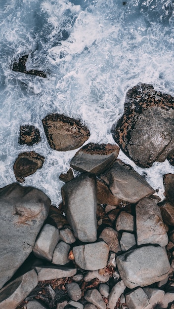 Vertical high angle shot of big stones in the stormy ocean water