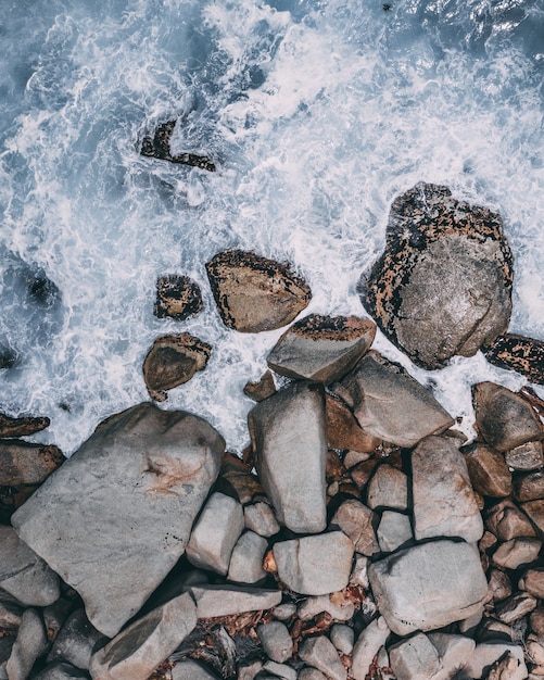 Vertical high angle shot of big stones in the stormy ocean water