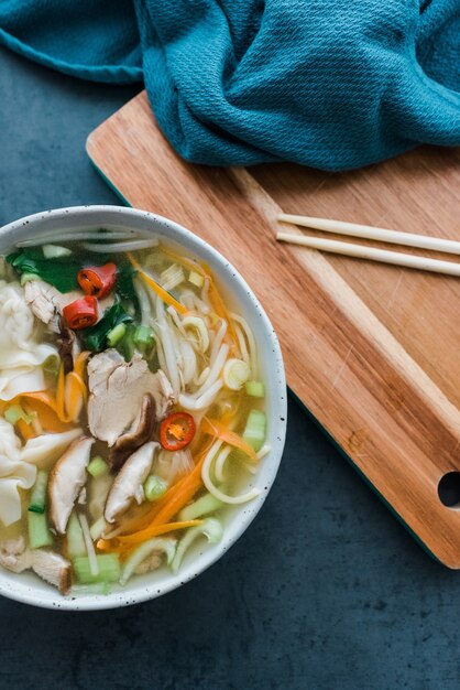 Vertical high angle shot of a bowl of noodles and meat next to some chopsticks on a table