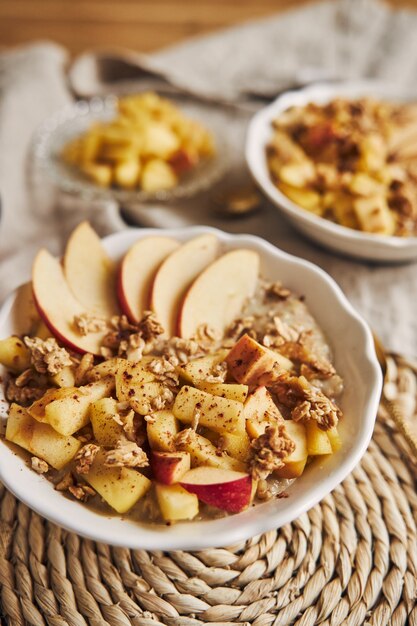 Vertical high angle shot of a bowl Porridge with cereal and nuts, and slices of apple on a table