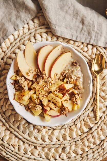 Vertical high angle shot of a bowl Porridge with cereal and nuts, and slices of apple on a table