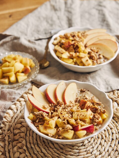 Vertical high angle shot of a bowl Porridge with cereal and nuts, and slices of apple on a table