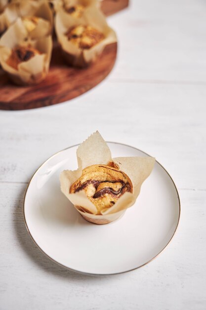 Vertical high angle shot of a delicious chocolate muffin near a wooden plate on a white plate