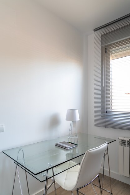 Vertical high angle shot of a minimalistic white room with a glass desk near the window