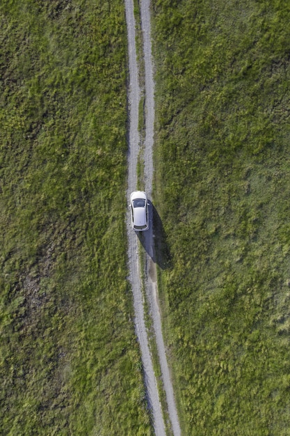 緑の谷の小道を通る白い車の垂直ハイアングルショット