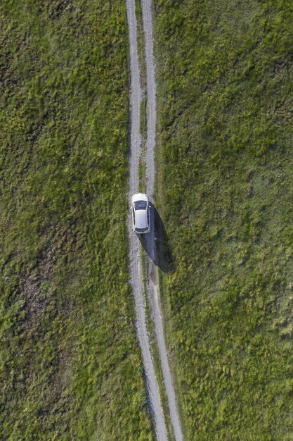 Vertical high angle shot of a white car riding through the path in the green valley