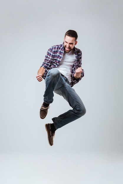 Вертикальное изображение бородатого мужчины в рубашке, который прыгает
