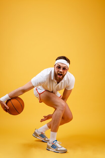 Вертикальное изображение бородатого спортсмена в солнцезащитных очках играет в баскетбол