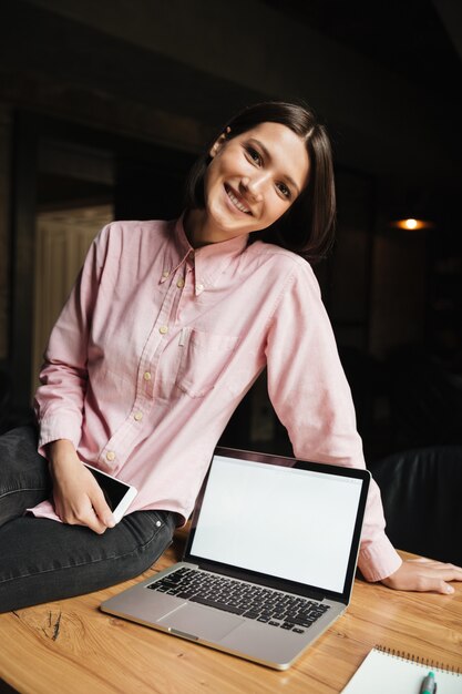 Vertical image of happy brunette woman sitting on table