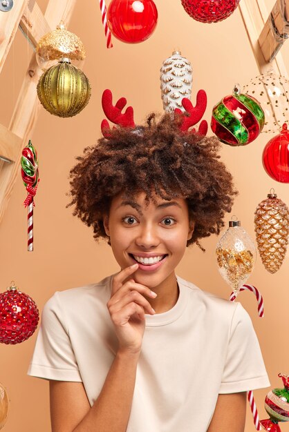 Vertical image of happy curly haired woman smiles broadly has perfect white teeth wears deer hoop and t shirt poses 