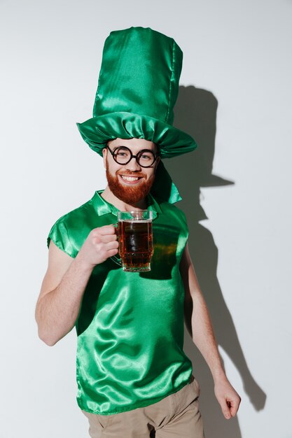 Вертикальное изображение счастливого человека в костюме st.patriks держа пиво