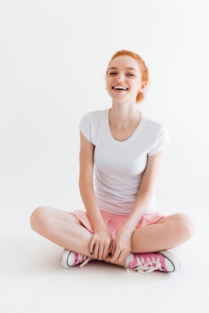 Vertical image of laughing ginger girl sitting on the floor and looking