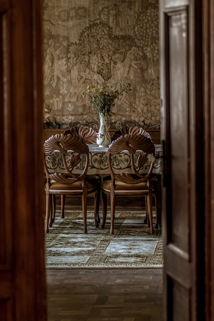 Foto gratuita l'immagine verticale di una lussuosa sala da pranzo con sedie ornate come si vede attraverso una porta aperta