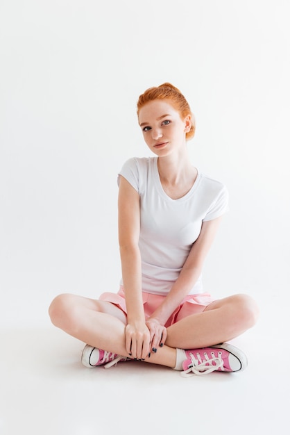 Vertical image of pretty ginger girl sitting on the floor and looking
