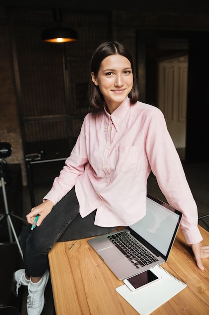 Free photo vertical image of smiling brunette woman sitting on table