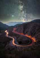 Бесплатное фото Вертикальный снимок дороги в горах под звездным небом с длительной выдержкой
