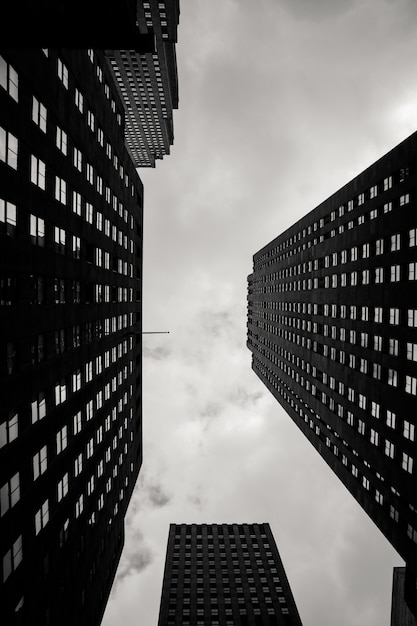 Vertical low angle grayscale of city buildings with a cloudy sky in the background