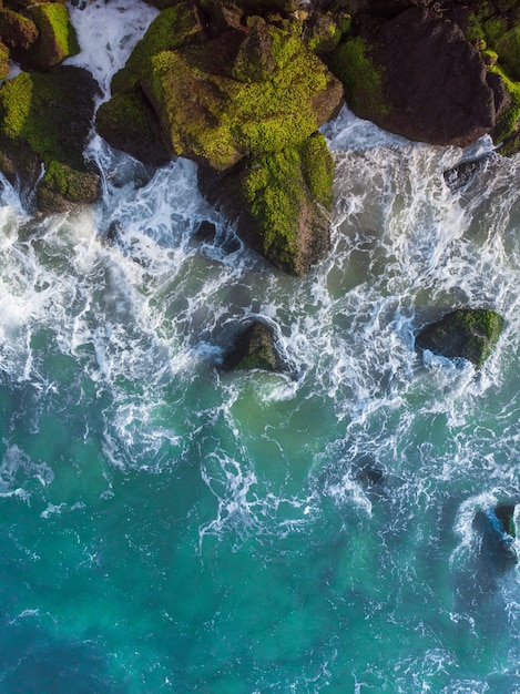 Free photo vertical overhead aerial shot of a wavy blue sea against the rocks