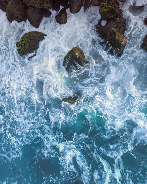 Vertical overhead aerial shot of a wavy blue sea against the rocks