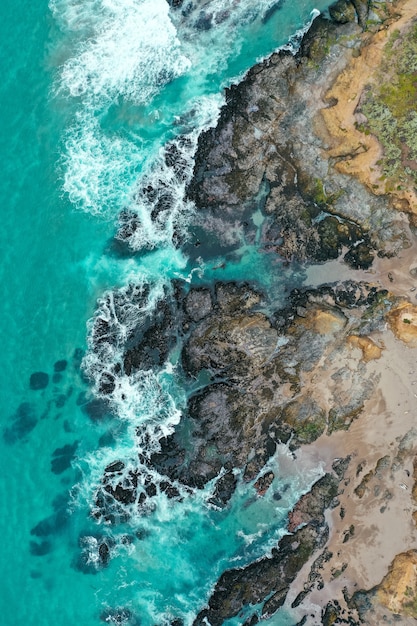 Vertical overhead shot of the beautiful shoreline of the sea with blue clean water and sandy beach