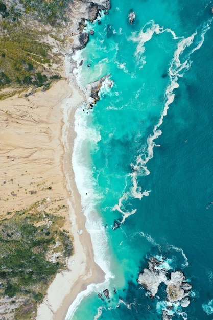 Vertical overhead shot of the beautiful shoreline of the sea with blue clean water and sandy beach