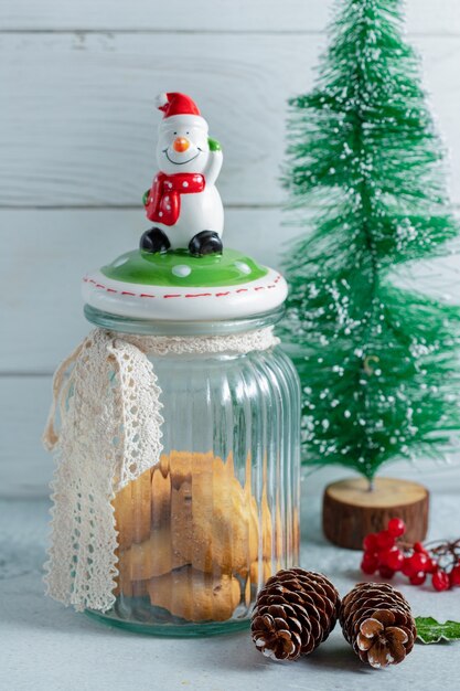 Вертикальное фото сливочного рождественского печенья в опарнике над серой поверхностью.