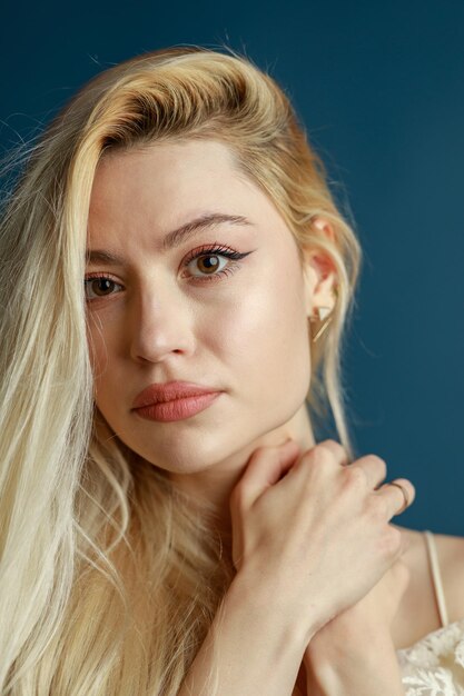 Vertical photo of cute blonde holding her hand to her neck and looking at the camera