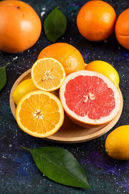 Vertical photo of fresh citrus fruits on wooden plate.