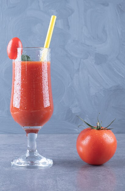 Вертикальное фото стекла свежего томатного сока и помидоров на сером фоне.