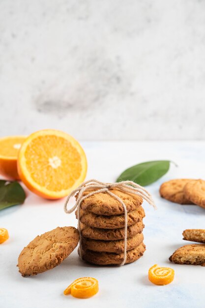 Vertical photo of homemade cookie and half cut orange with leaves over white wall.