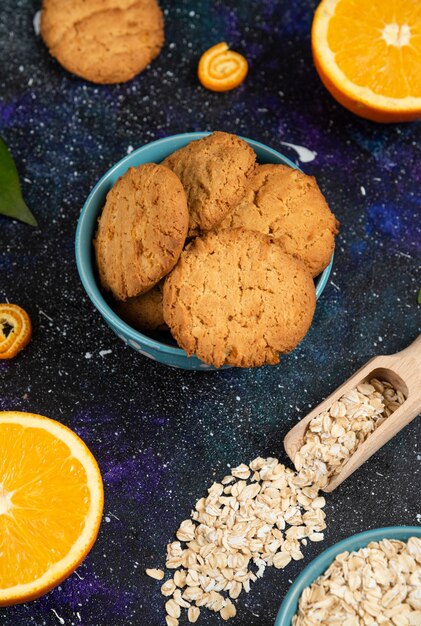 Vertical photo of homemade cookies in bowl and orange with oatmeal over ground. 