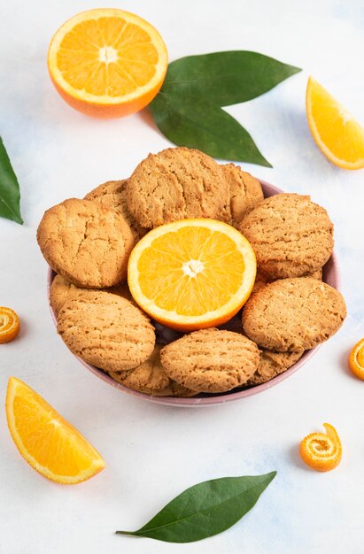 Вертикальное фото домашнего печенья с наполовину разрезанным апельсином в миске.