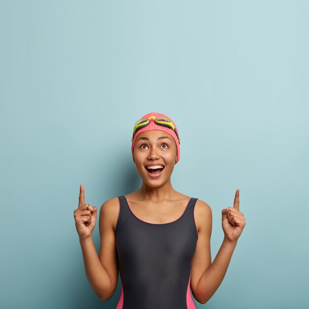 Vertical photo of joyous dark skinned female enjoys favourite hobby and summer active rest, dressed in swimsuit