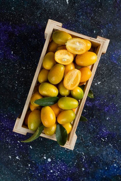 Vertical photo of Organic kumquats in wooden box over blue surface