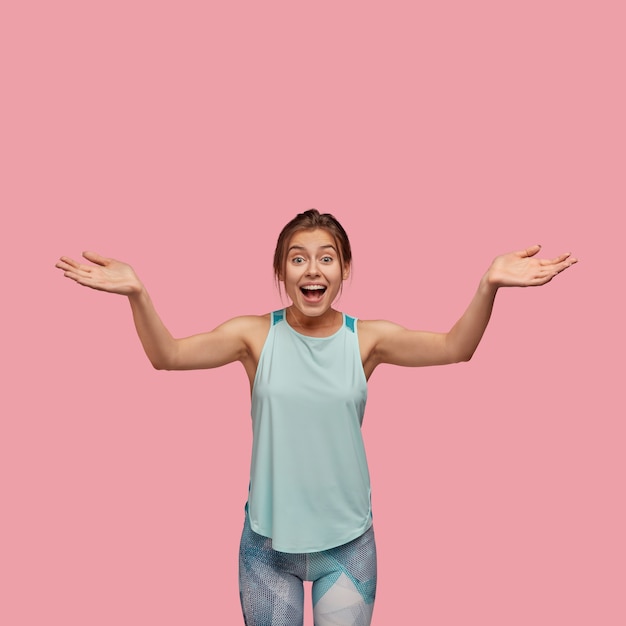 Vertical photo of overjoyed beautiful young woman spreads hands with joy