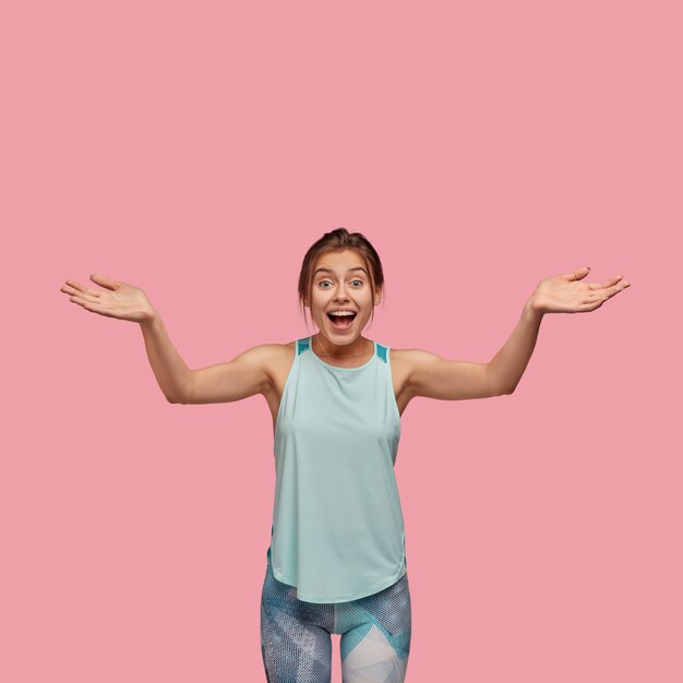 Vertical photo of overjoyed beautiful young woman spreads hands with joy