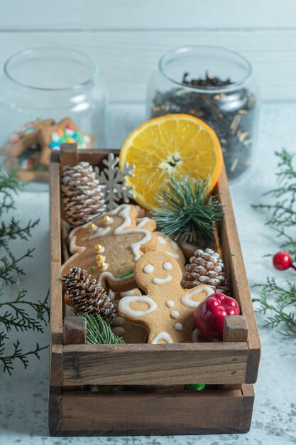 Vertical photo of wooden box full with snacks. Homemade cookies and orange slice with pine cones.