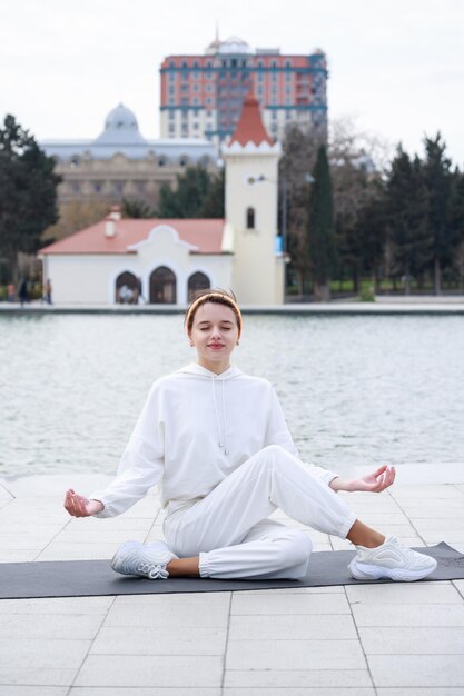 Vertical photo of young athlete sitting on yoga mat and doing meditation at the park High quality photo
